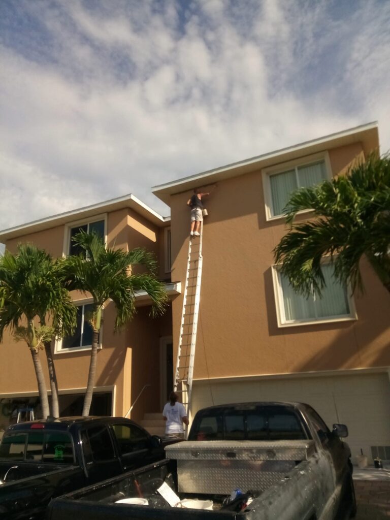 Miller's Pressure Washing employee on a 40 foot ladder painting the cut-in of the stucco wall at the top of the third story. There are a lot of cars in the parking lot that prevented us spraying the building.